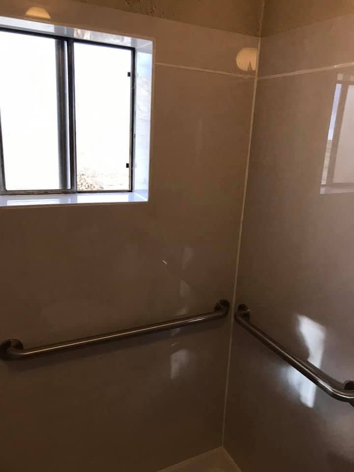 Empty tiled shower with stainless steel grab bars and a small window.