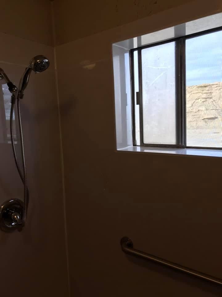 Shower stall with chrome showerhead, grab bar, and small window letting in daylight.