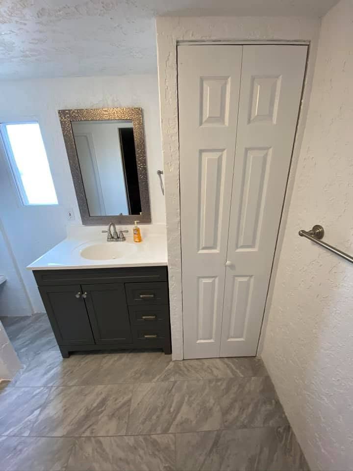 Small bathroom vanity with mirror, white closet door, gray tile floor, and towel bar on the wall.