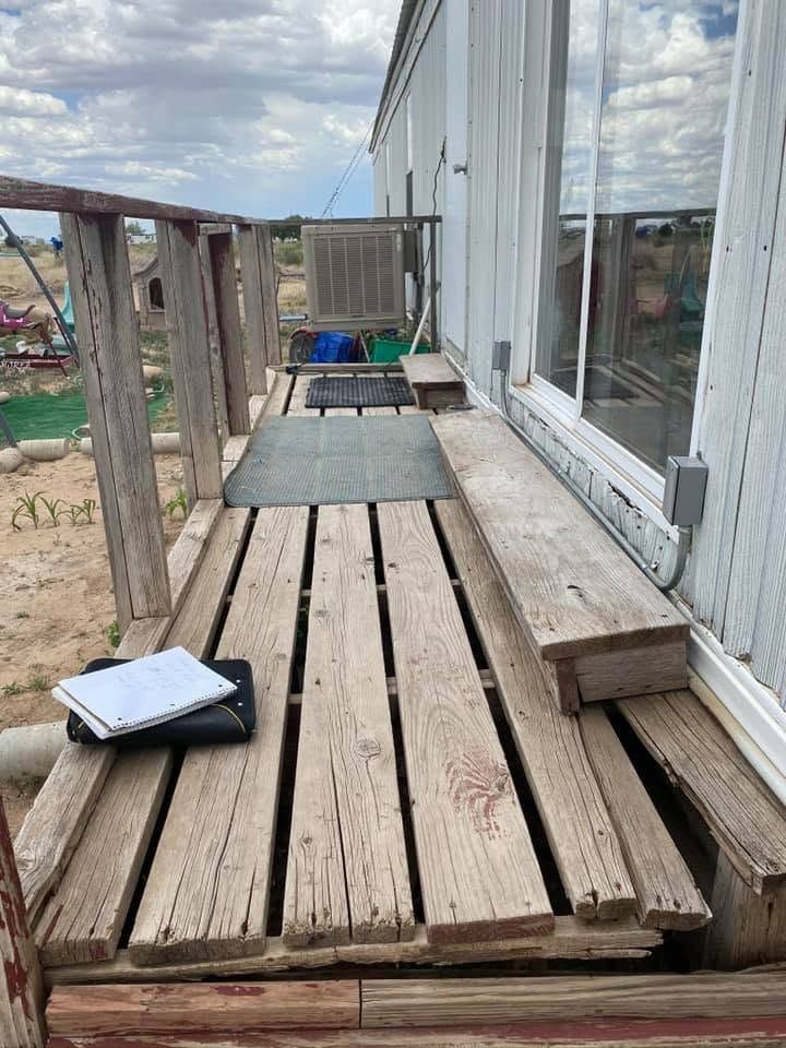 Weathered wooden deck beside a building, with two gray mats and a notebook on the planks.