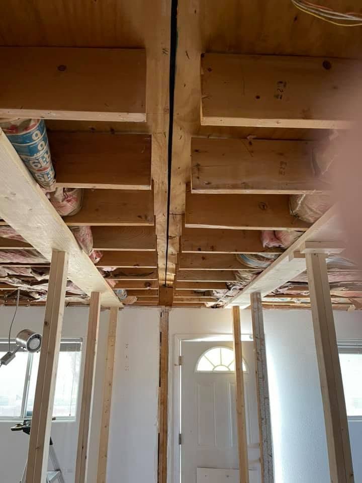Renovation site showing exposed wooden ceiling joists above a hallway with white walls and doorframes