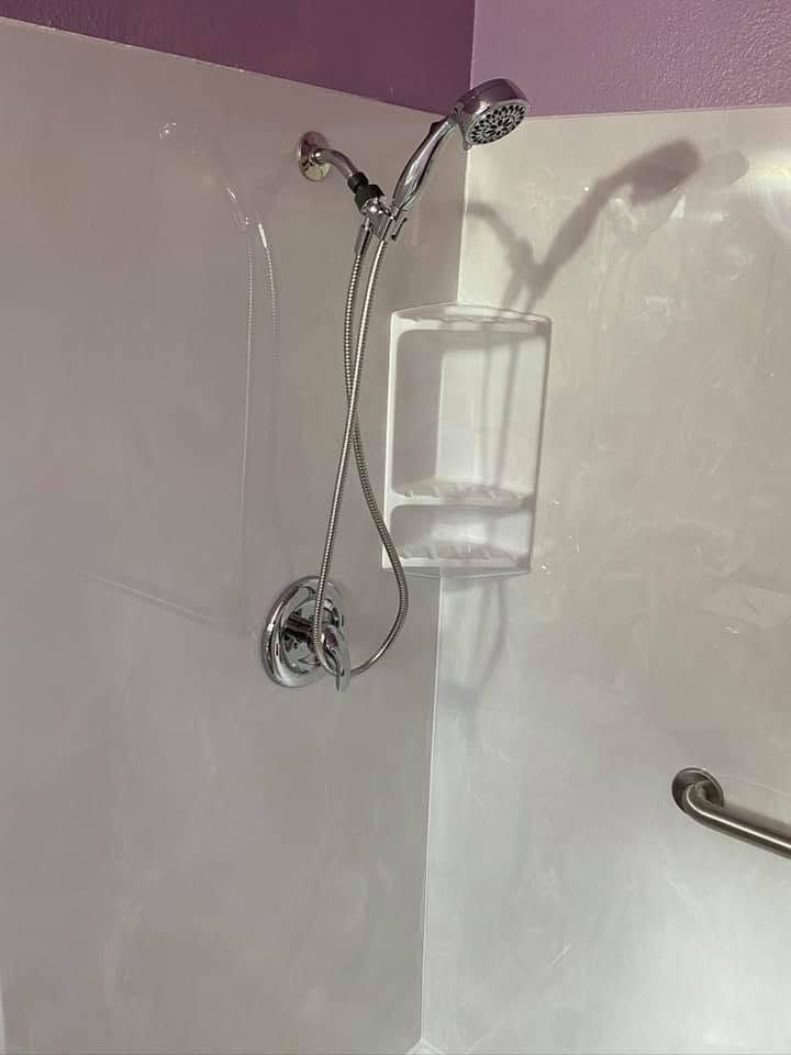 Shower wall with chrome handheld showerhead, hose, and mounted clear soap dispenser.