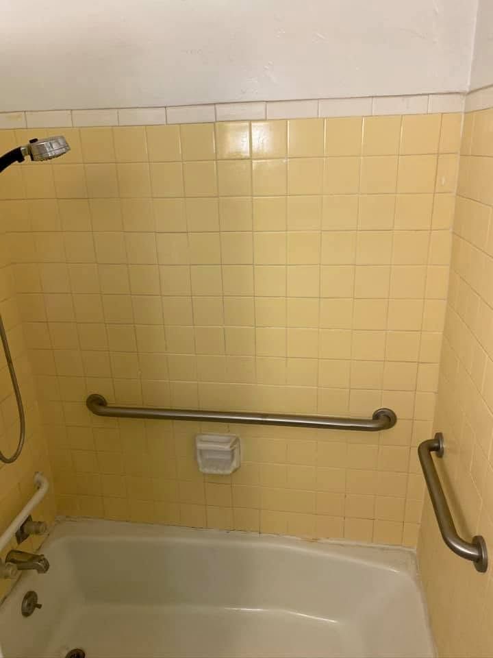 Bathroom with yellow tile shower-tub, horizontal grab bars, and handheld showerhead