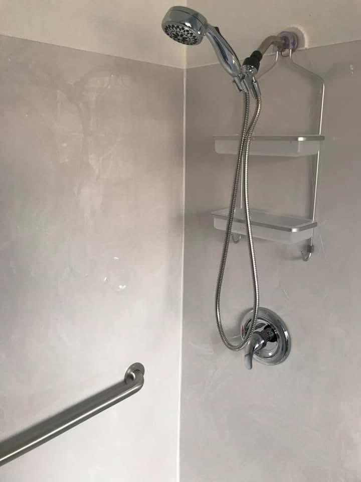 Shower stall with handheld showerhead, grab bars, and a wall shelf in a white bathroom
