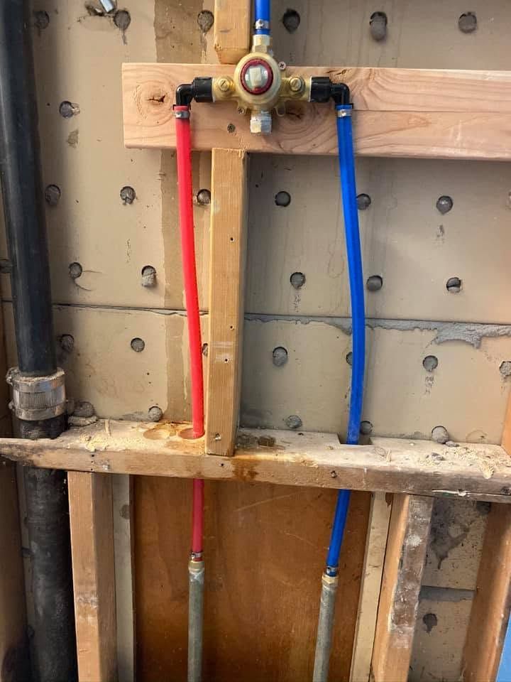 Exposed red and blue water pipes with valves in an unfinished wall