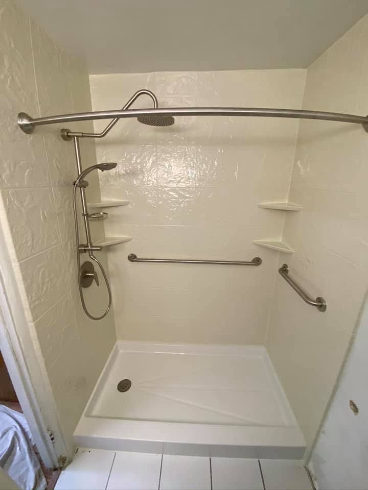 Accessible shower stall with grab bars, handheld shower, built-in corner shelves, and a low curb.