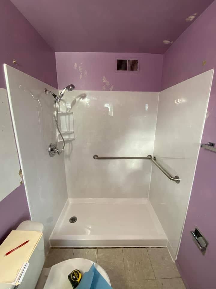Small bathroom shower stall with white tile, purple walls, grab bar, and wall-mounted showerhead.
