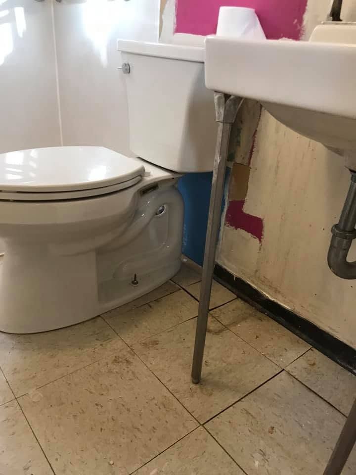 Small bathroom with a toilet beside a sink and exposed plumbing under the vanity.