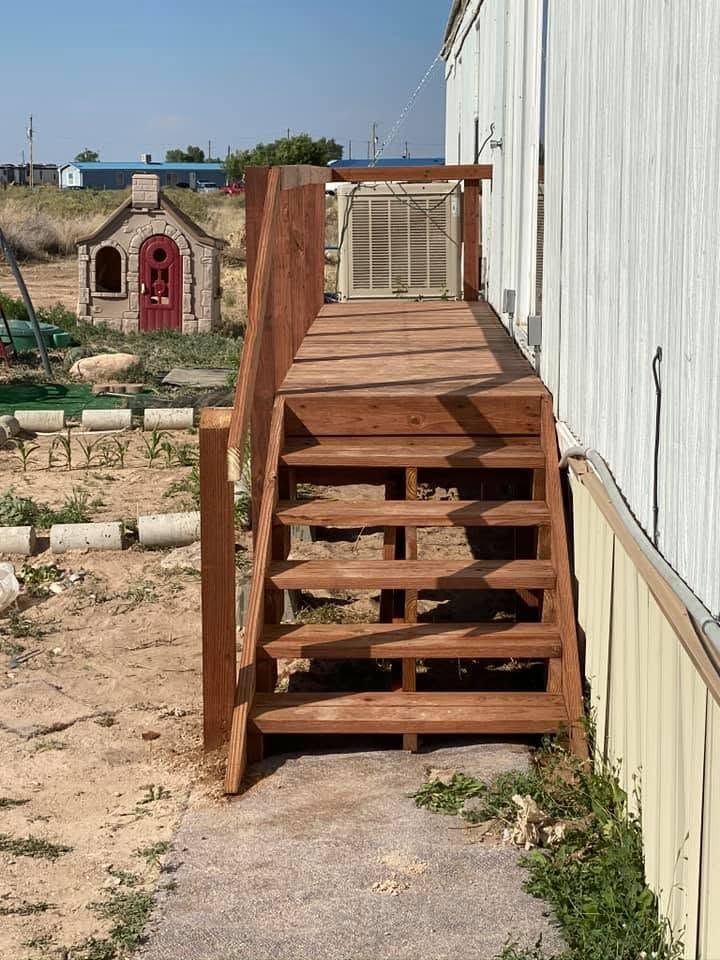 Wooden outdoor staircase with railing beside a white building, leading up to a deck.