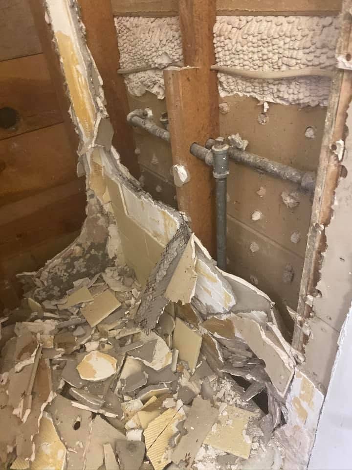 Damaged interior wall with exposed studs, broken drywall, and debris on the floor