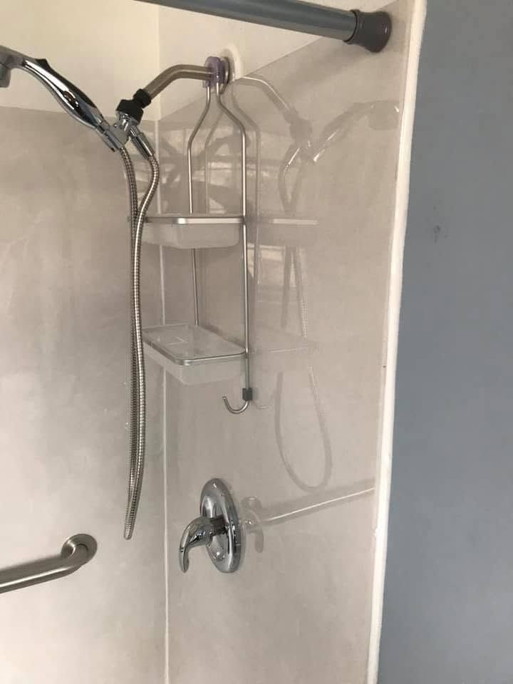 Walk-in shower with handheld showerhead, wall-mounted caddy, and grab bars on tiled walls