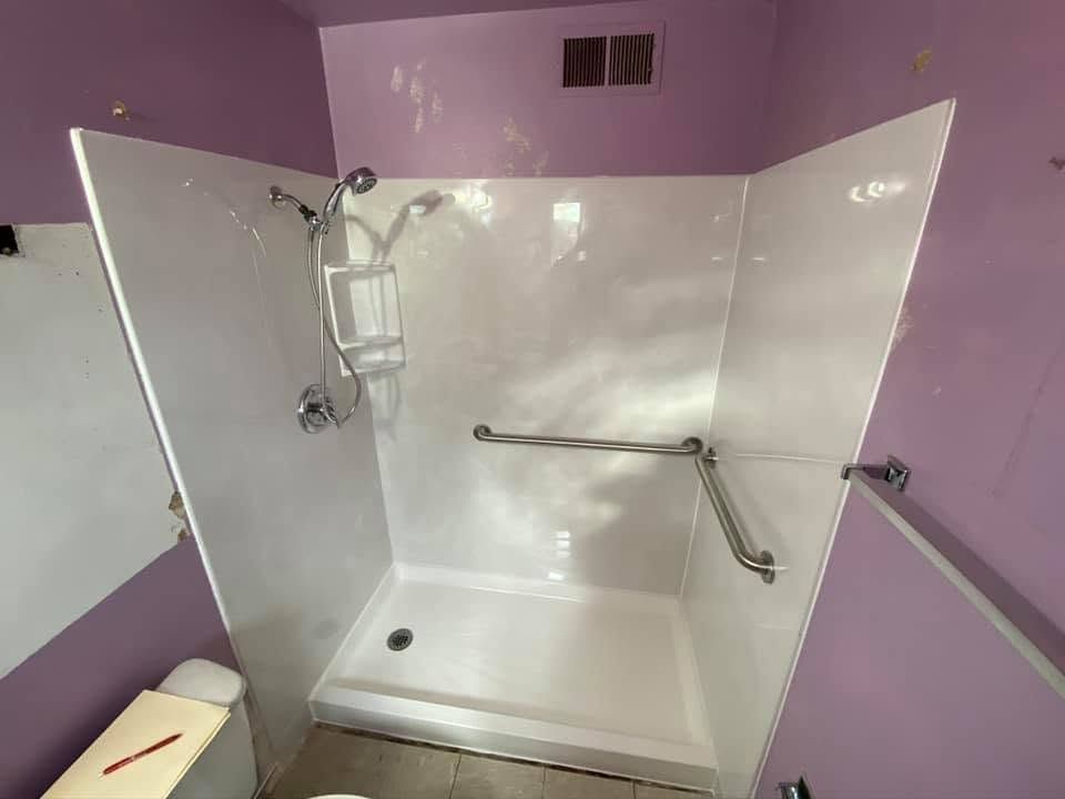 Accessible shower stall with white doors, grab bars, and a shower chair in a purple bathroom