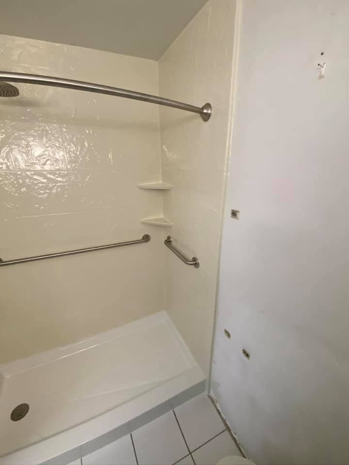 Accessible bathtub with grab bars, built-in seat, and white tiled walls in a small bathroom