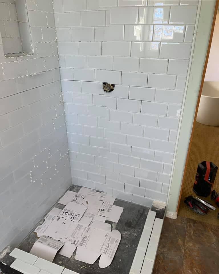 Small white-tiled shower under renovation with tools and tile pieces on the floor.