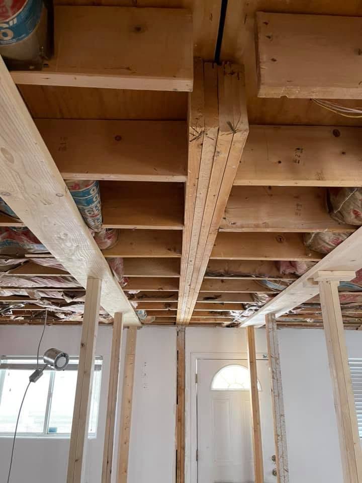 Exposed ceiling joists and beams inside a room under construction, with light fixtures and windows below