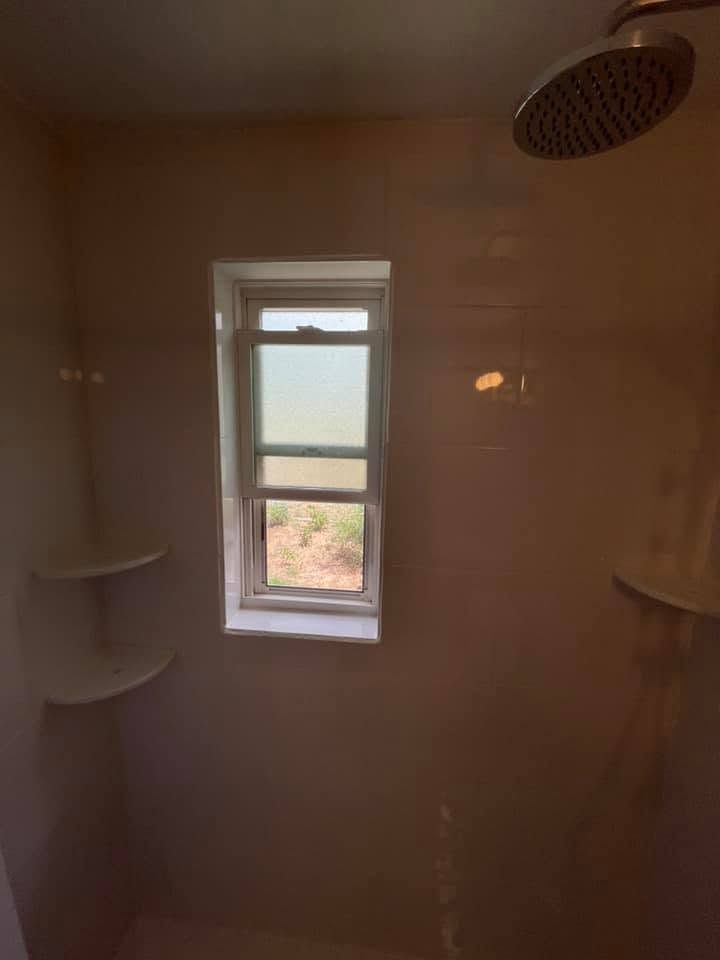 Small shower stall with white shelves, a window, and a ceiling showerhead.