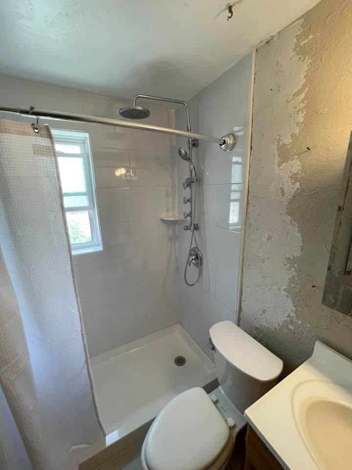Small bathroom with shower stall, toilet, sink, and exposed wall repair area
