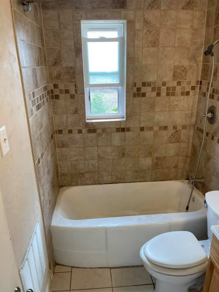 Small beige-tiled bathroom with a bathtub, toilet, and window.