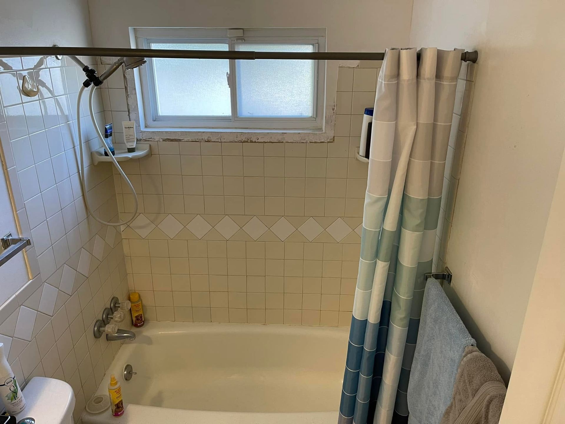 Small bathroom with a bathtub, tiled walls, a frosted window, and a striped shower curtain.