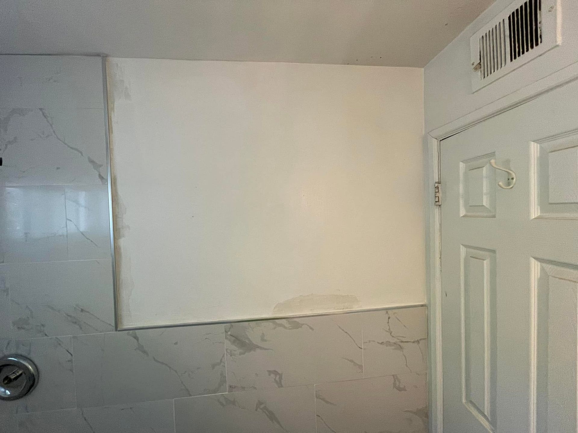 Bathroom wall with a blank white panel above gray marble-patterned tiles near a shower door