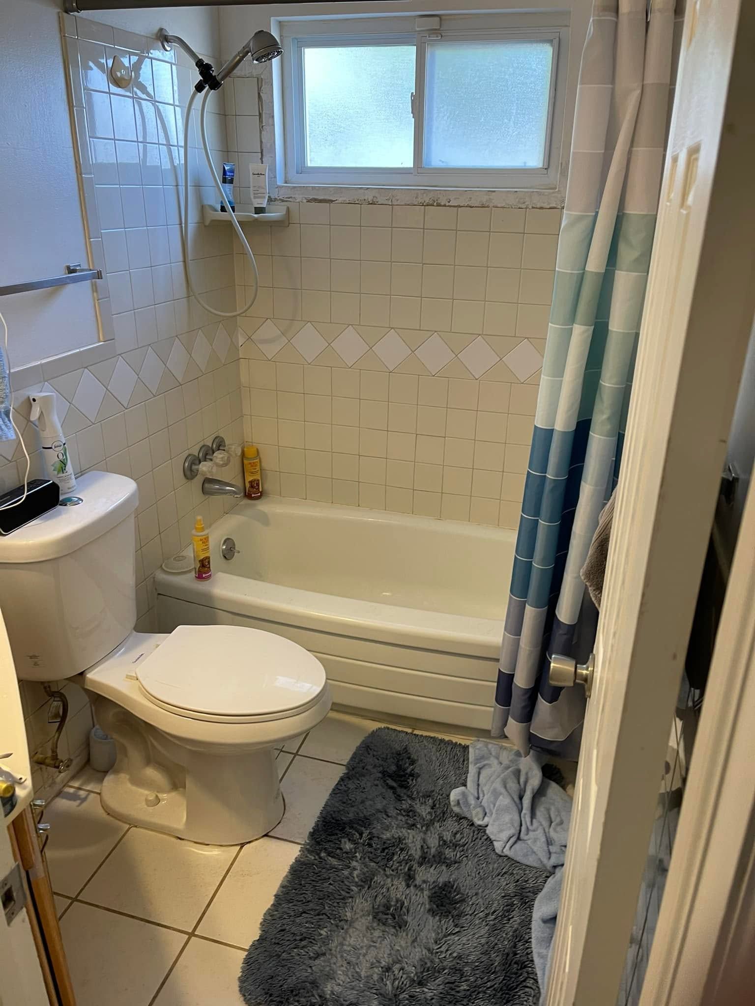Small bathroom with toilet, sink, bathtub, shower curtain, and window above the tub.