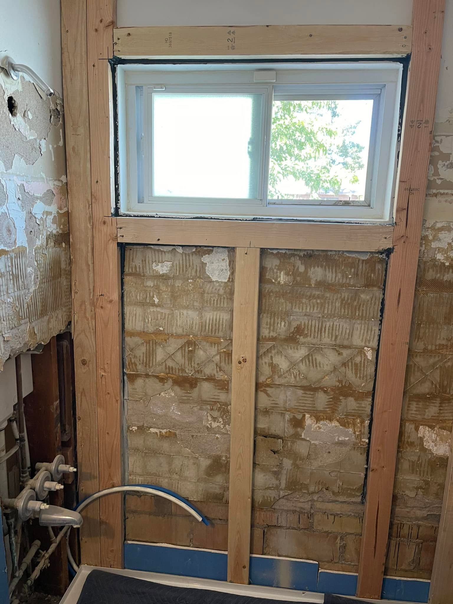Partially renovated wall with exposed insulation and a small window above the framing