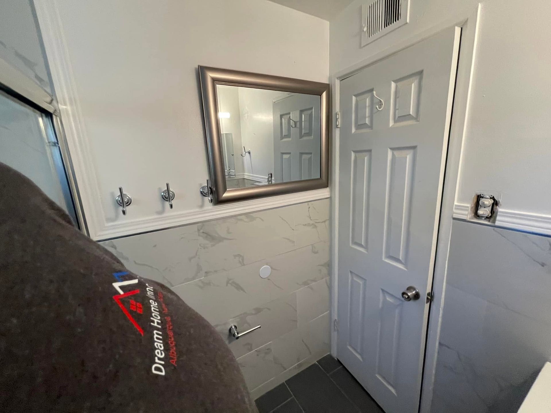 Bathroom with white door, mirrored cabinet, tiled walls, and a trash bin in the foreground