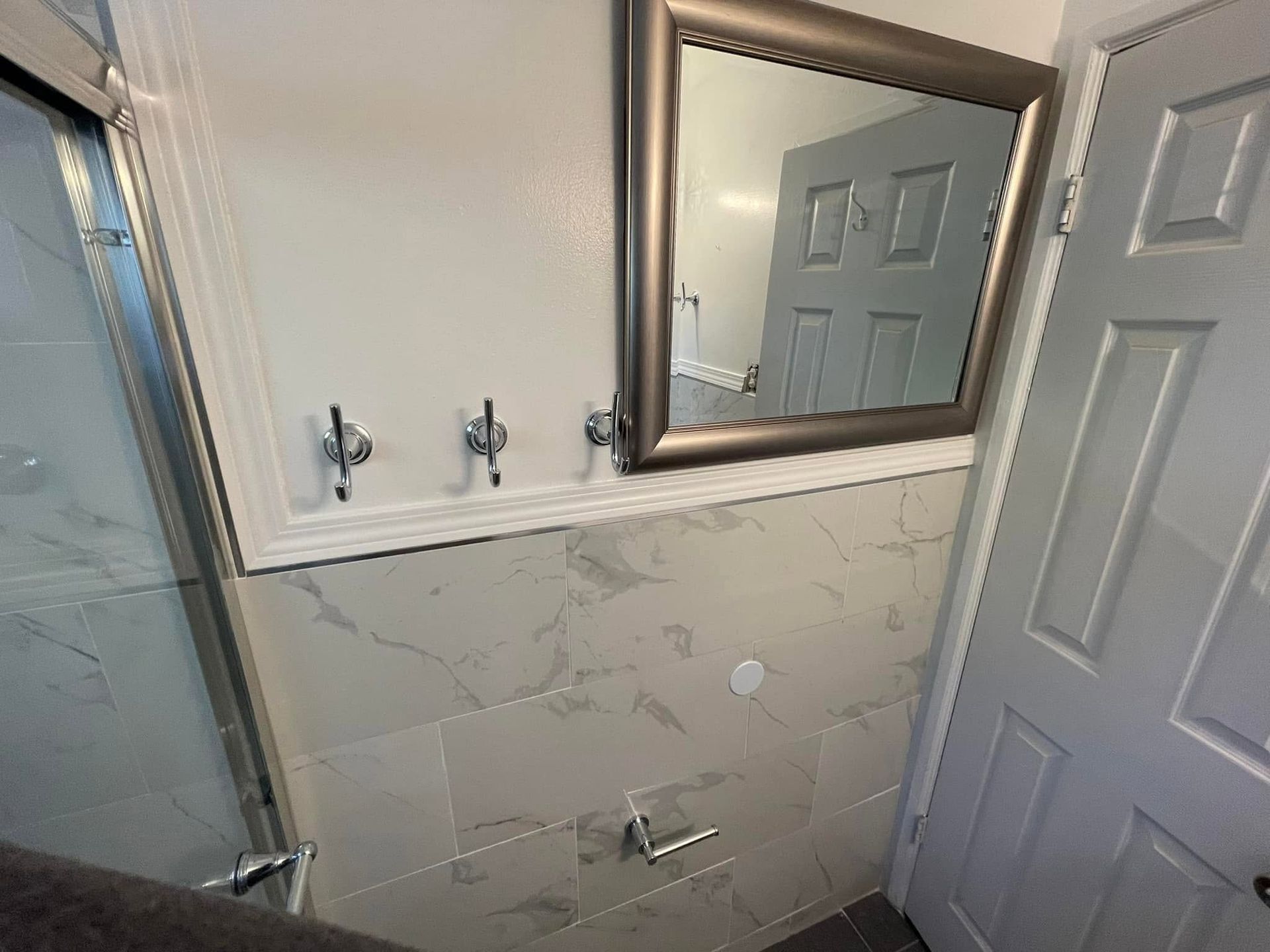 Small bathroom vanity area with mirrored cabinet, white marble-look tiles, and a shower door visible on the left.