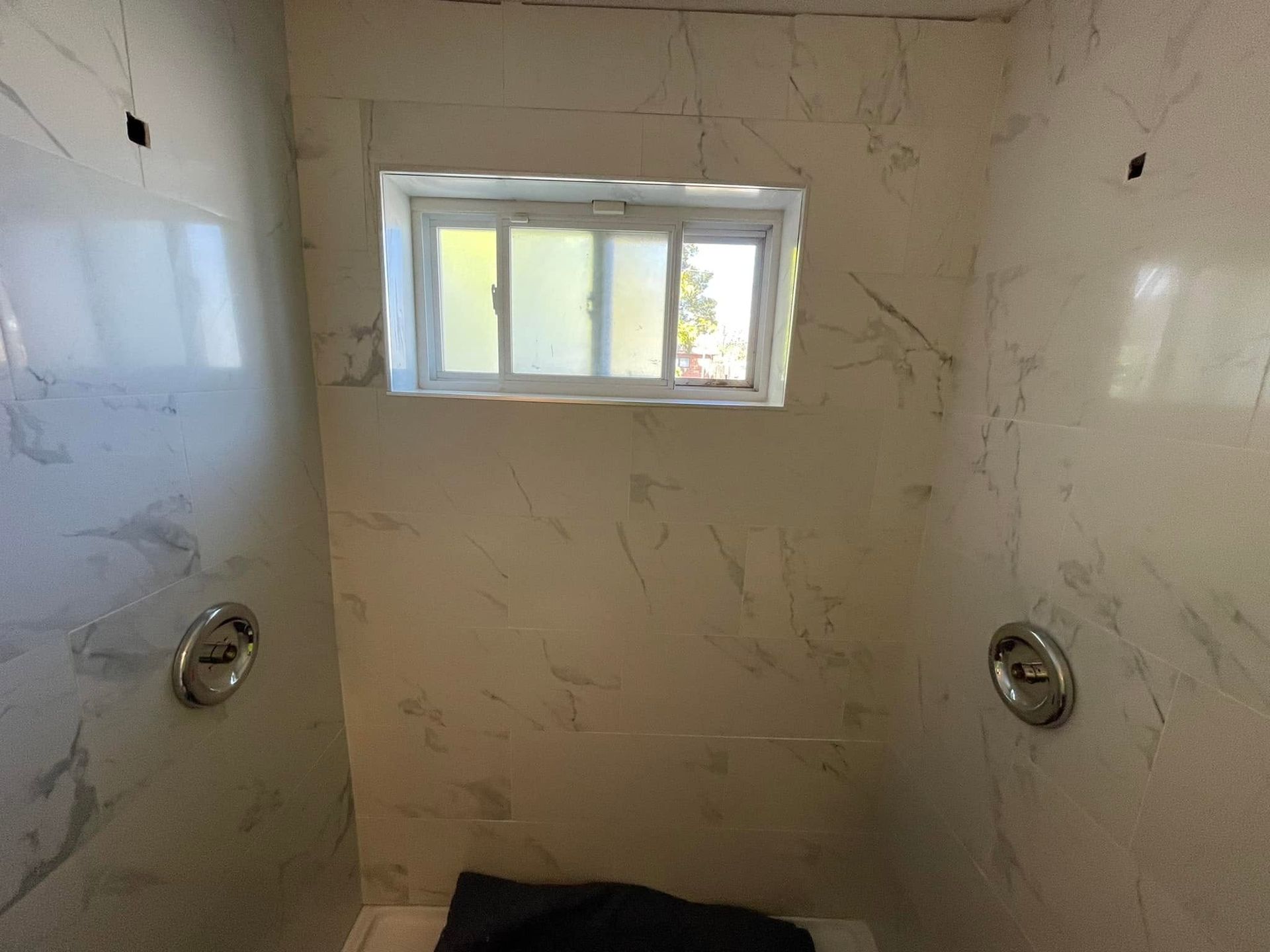 Empty tiled shower with a small frosted window above the tub area.
