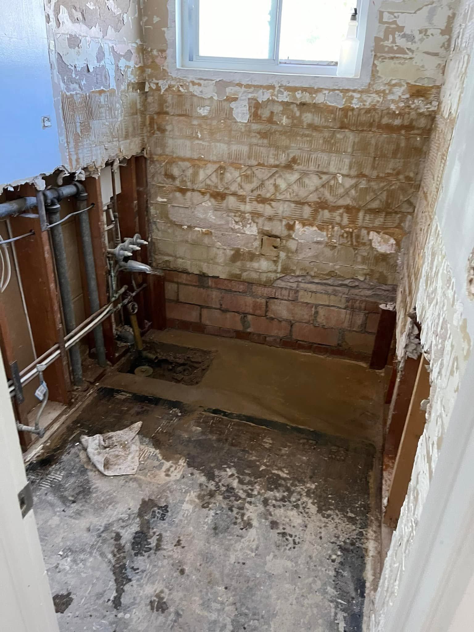 Small unfinished bathroom with exposed plumbing, peeling walls, and a window.