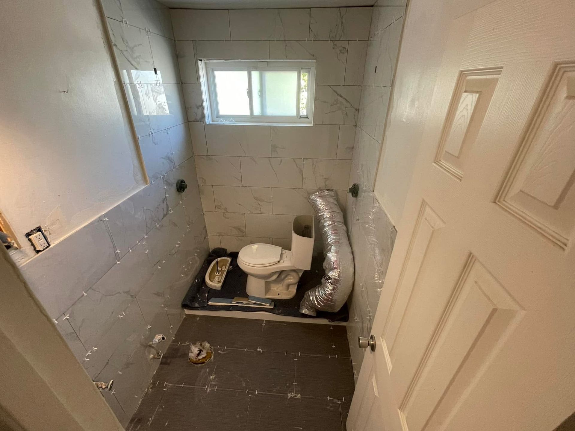 Small unfinished bathroom with a toilet, window, exposed duct, and bare walls.