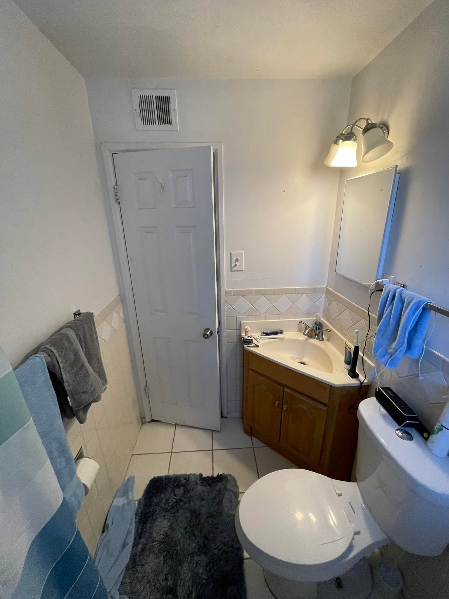 Small white bathroom with sink, toilet, shower curtain, wall mirror, and towels hanging on the left.