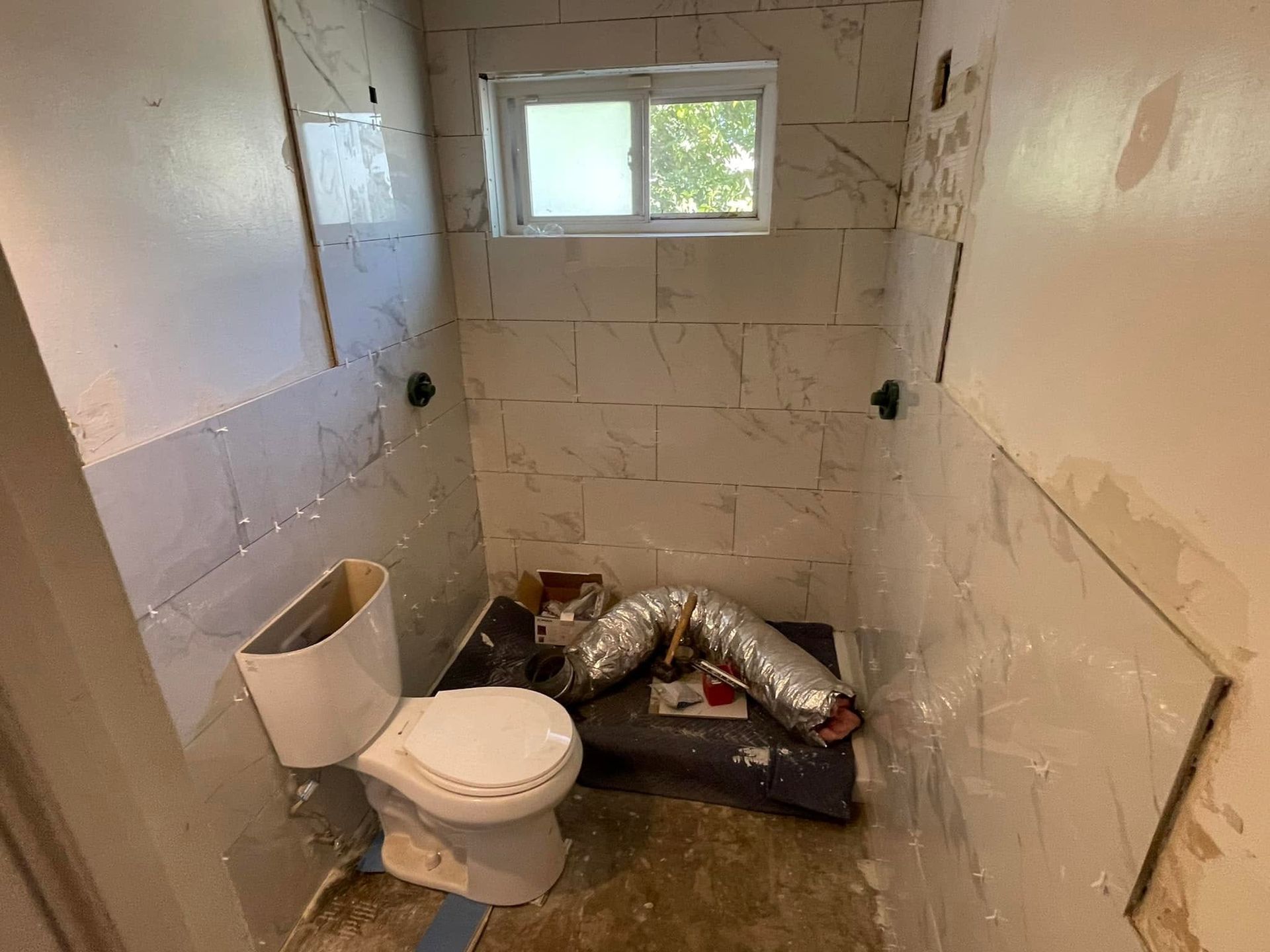 Small bathroom under renovation with tiled walls, toilet, and construction debris on the floor.
