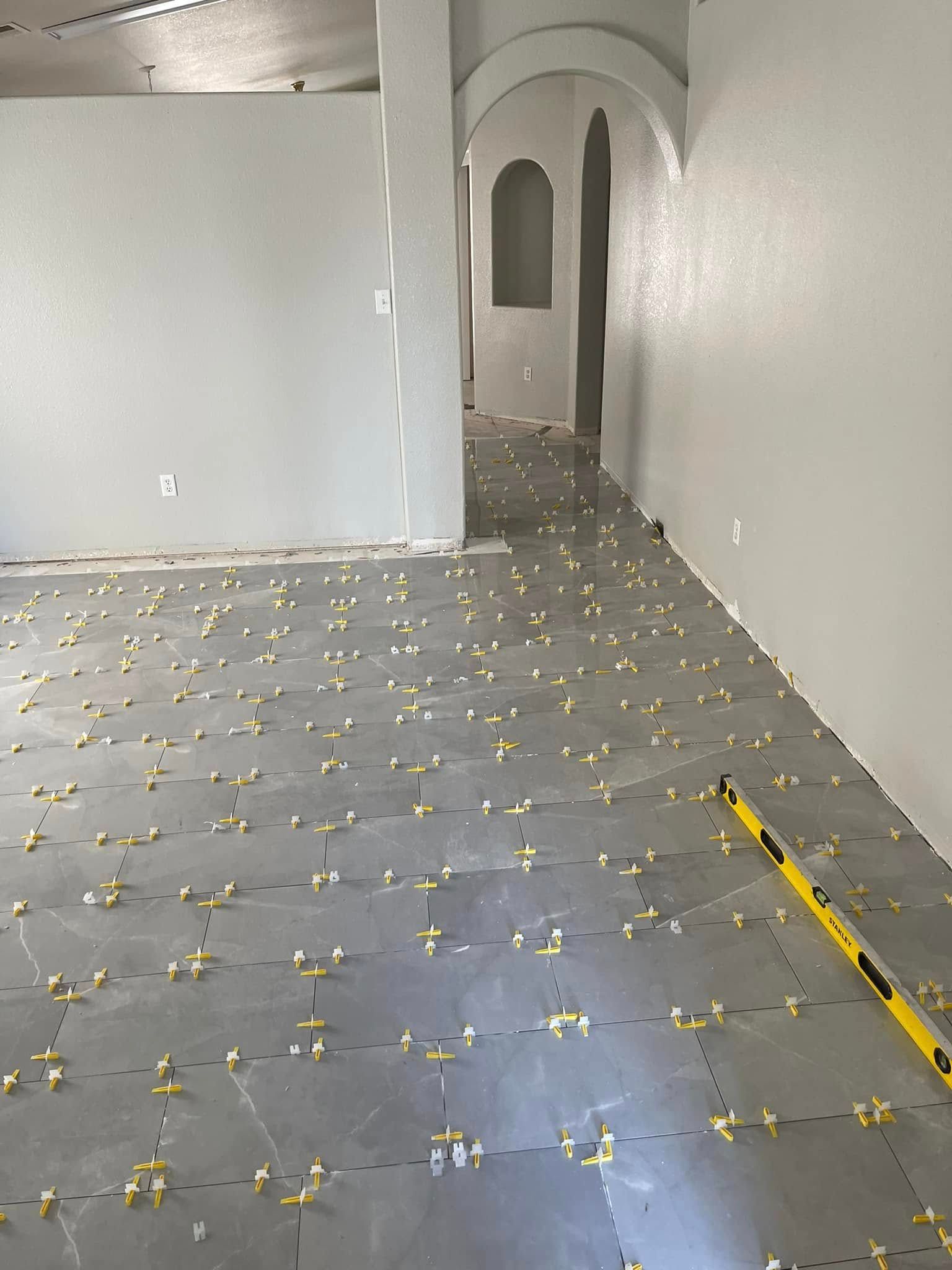Empty white room with gray tiled floor and arched doorway in the back; yellow tape marks the floor edge.