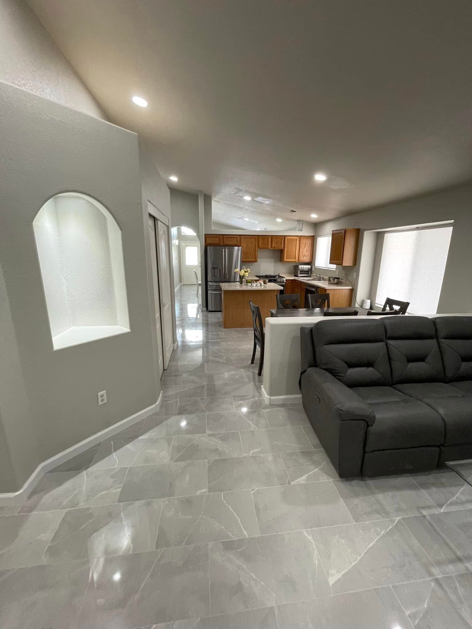 Modern open-concept living room with gray sectional, tile floor, and view into the kitchen.
