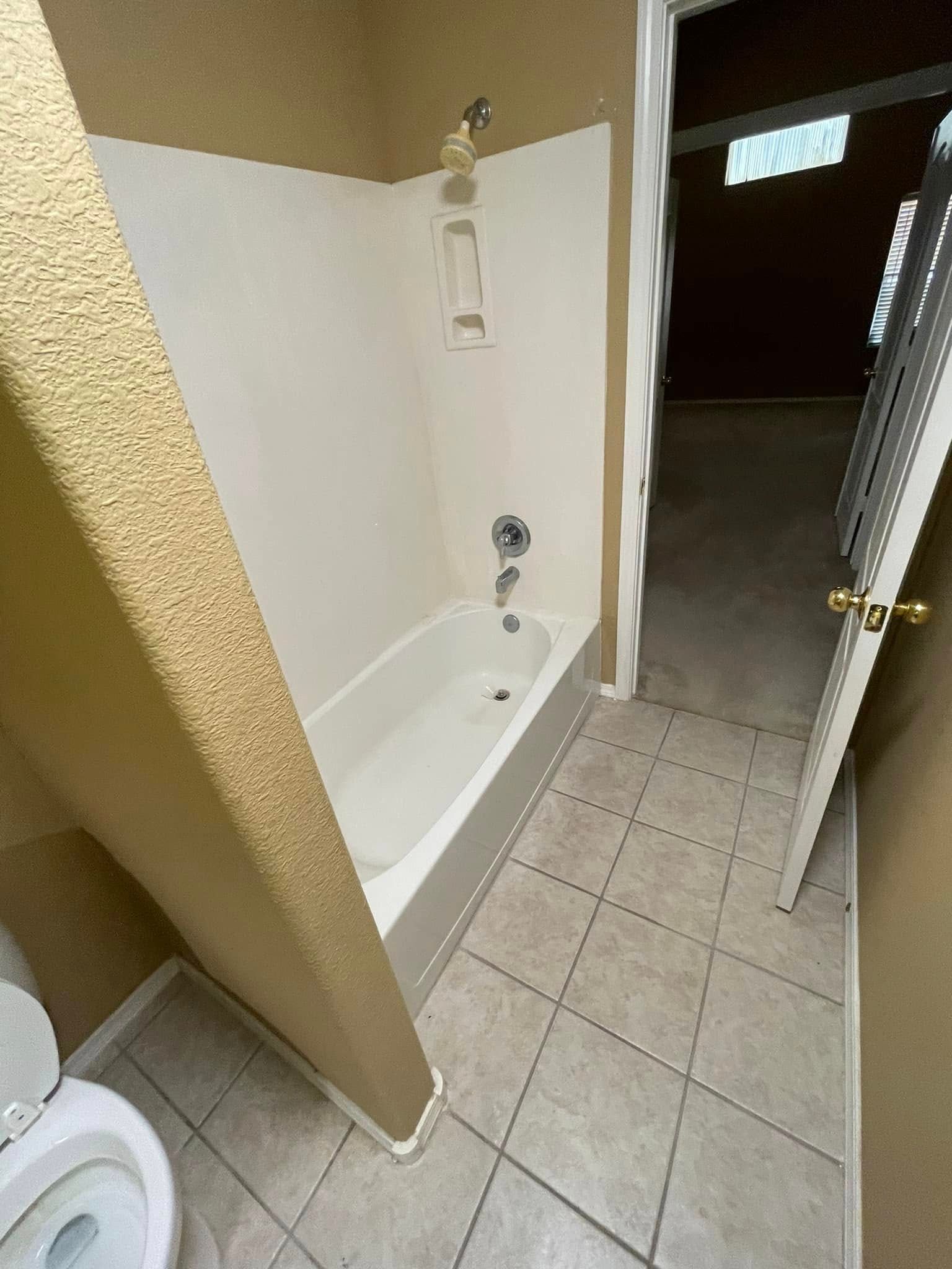 Small tiled bathroom with a white bathtub, beige walls, and an open door to a hallway.