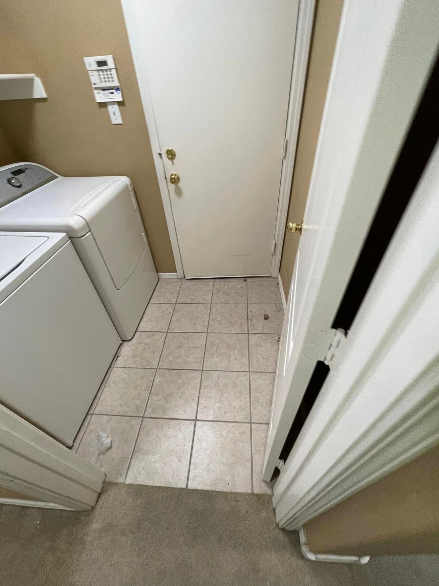 Narrow laundry room hallway with a washer on the left, tiled floor, and a closed door ahead.