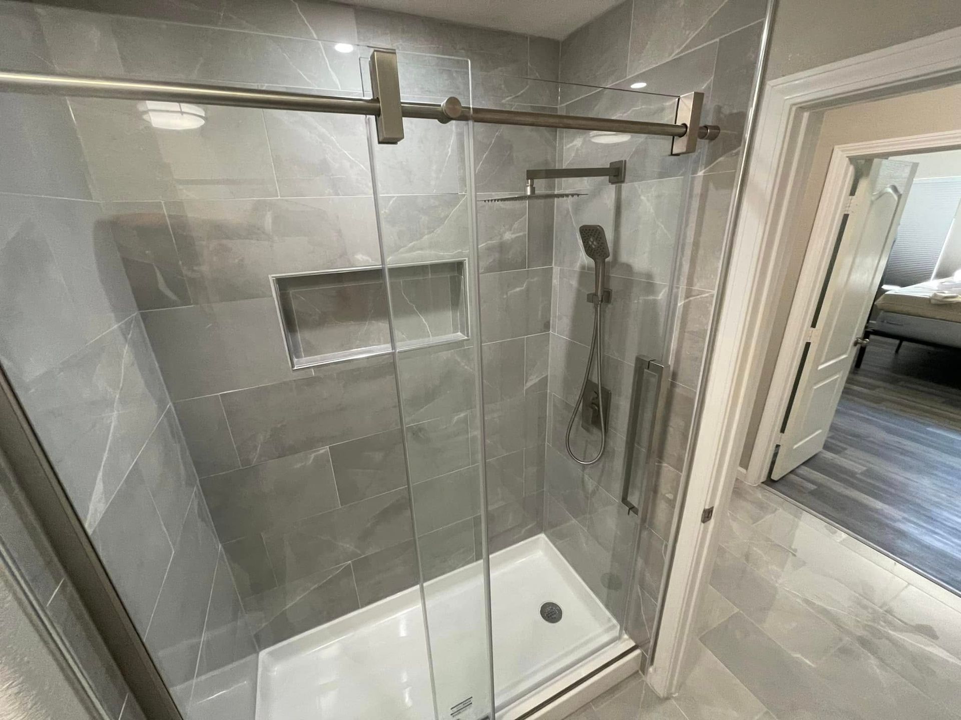Walk-in shower with gray tile walls, glass door, built-in niche, and white shower base.