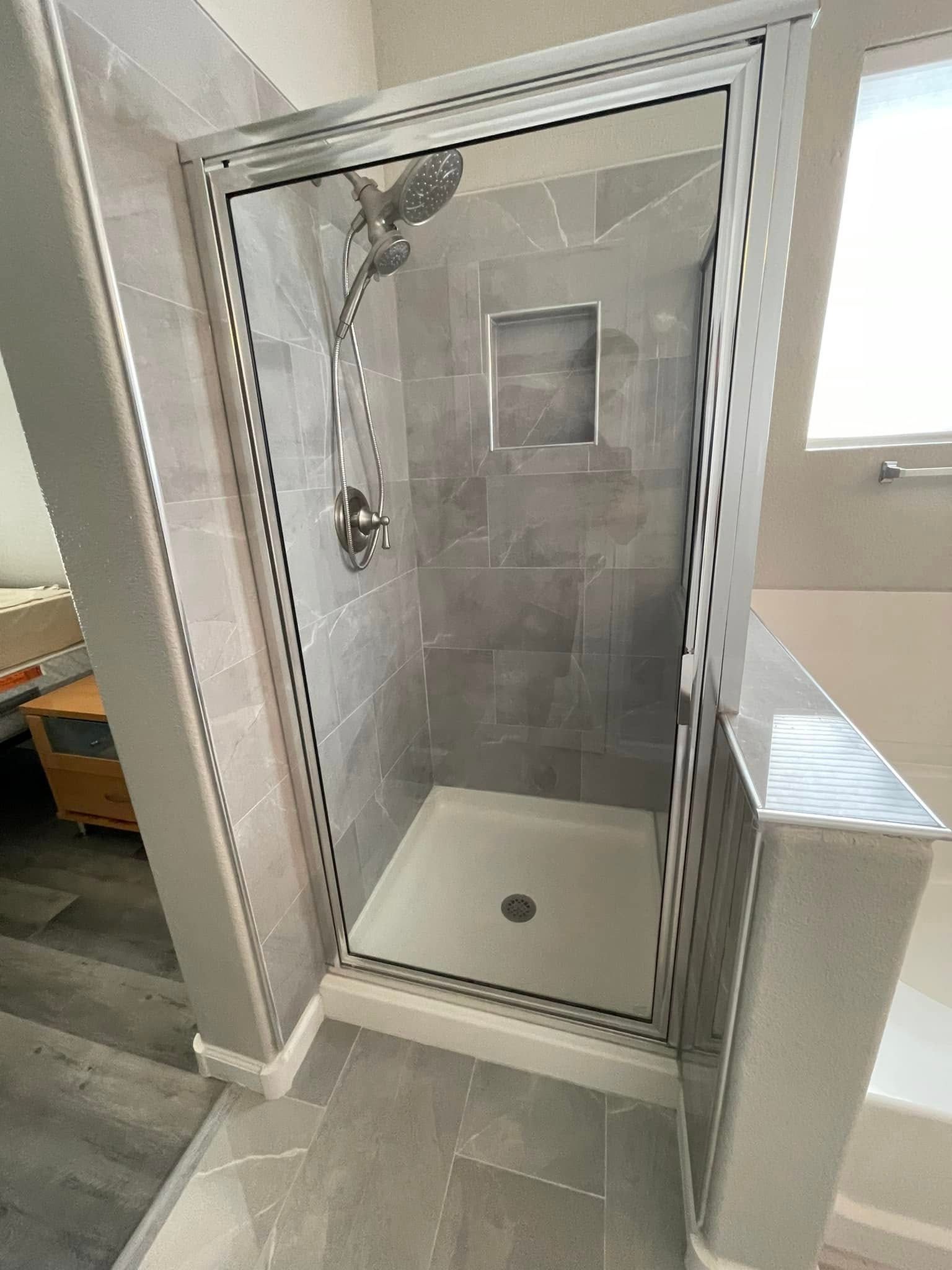 Small accessible shower stall with grab bars, handheld showerhead, and gray tile in a tiled bathroom