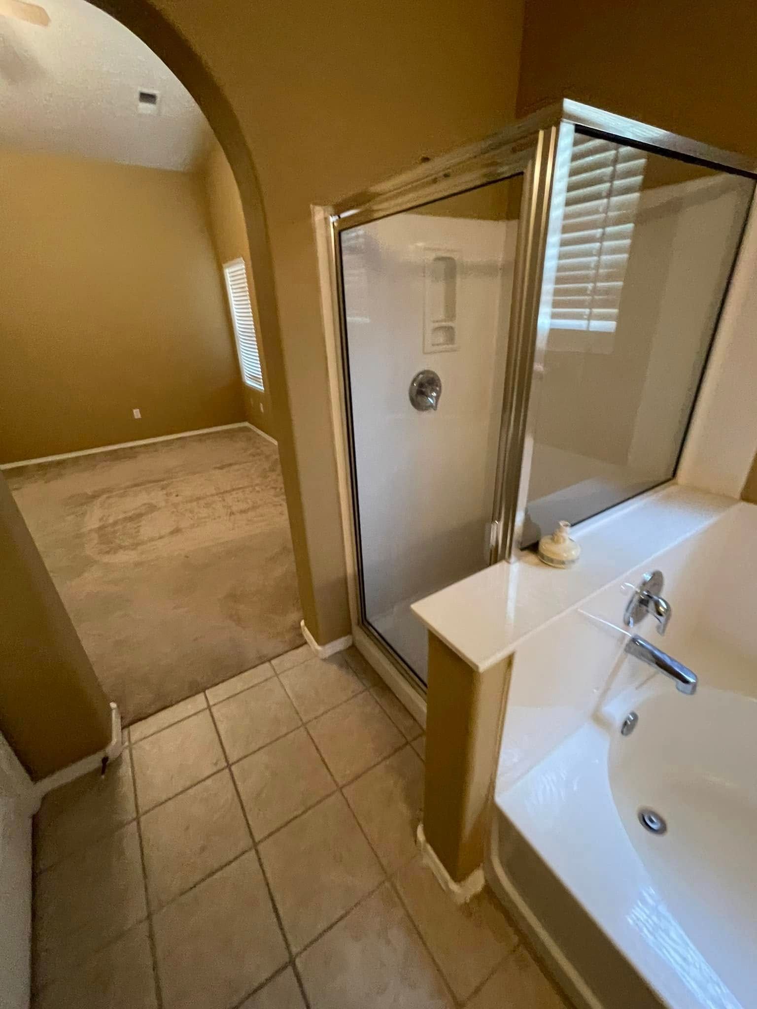 Bathroom with white tub and sink, tan tiled floor, and an open doorway to a carpeted room.