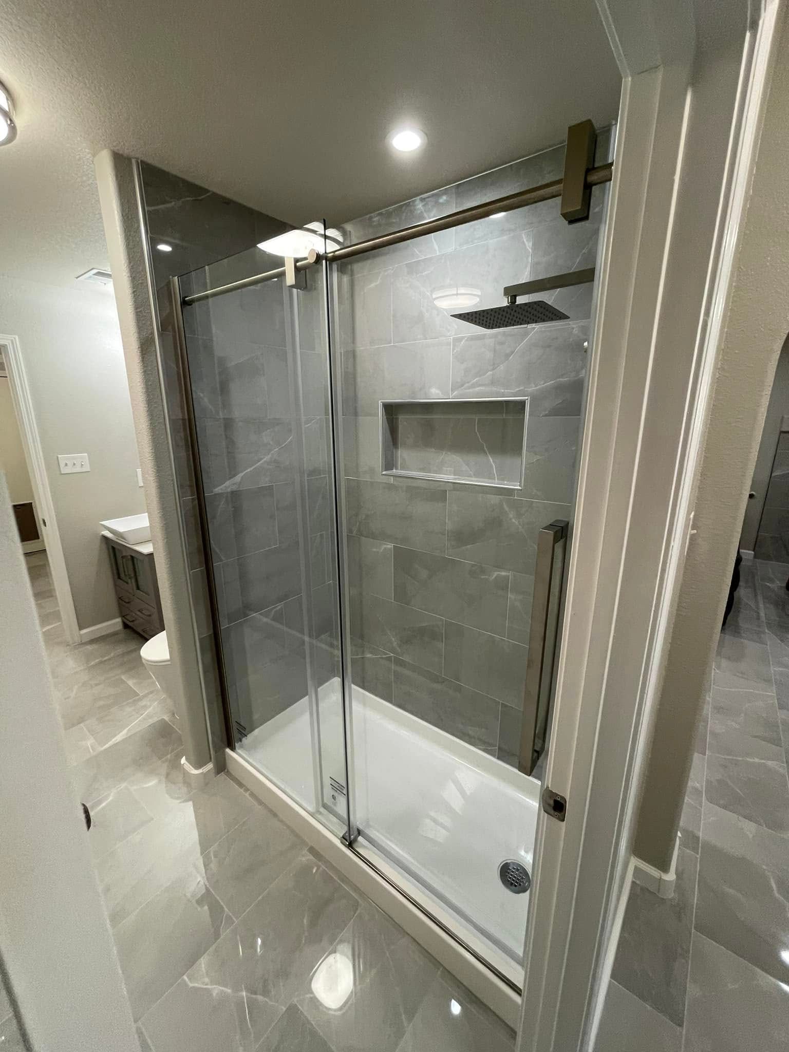 Glass shower enclosure with chrome frame and gray tiled bathroom walls.