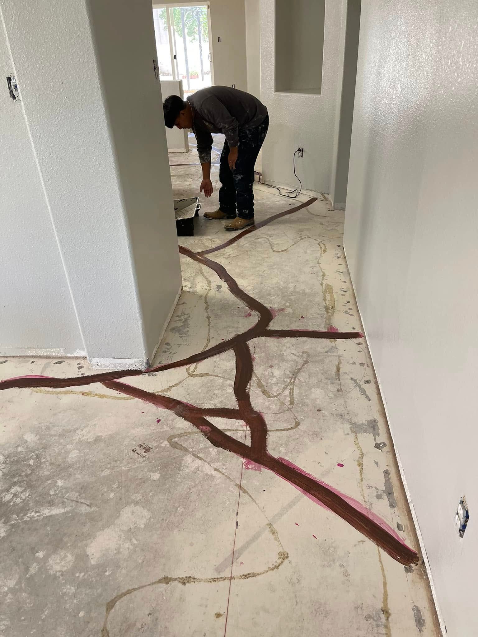 Person crouching in a hallway, applying dark red epoxy-like material to cracks in the floor.