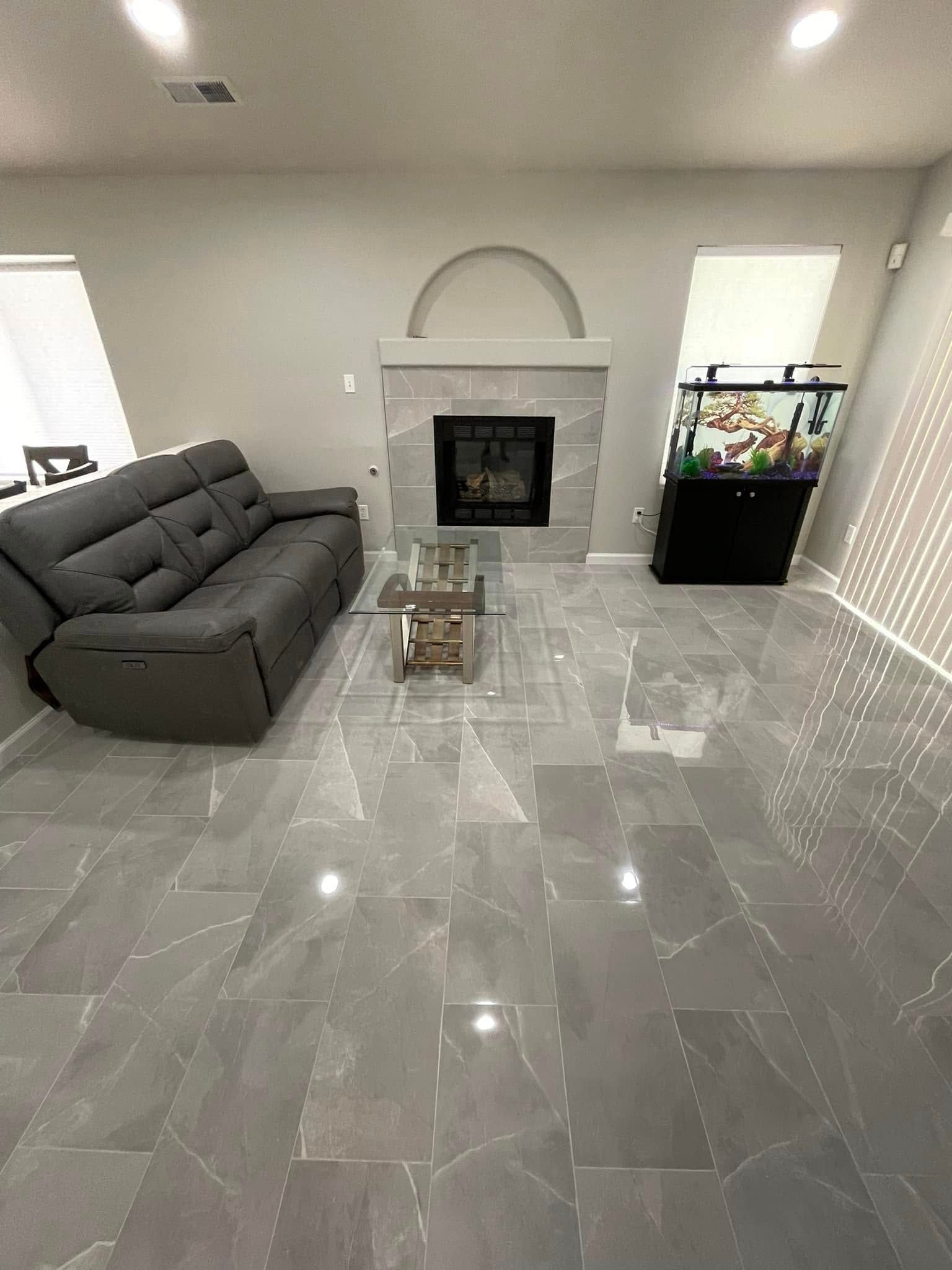 Modern living room with gray sectional, marble floors, fireplace, and fish tank.