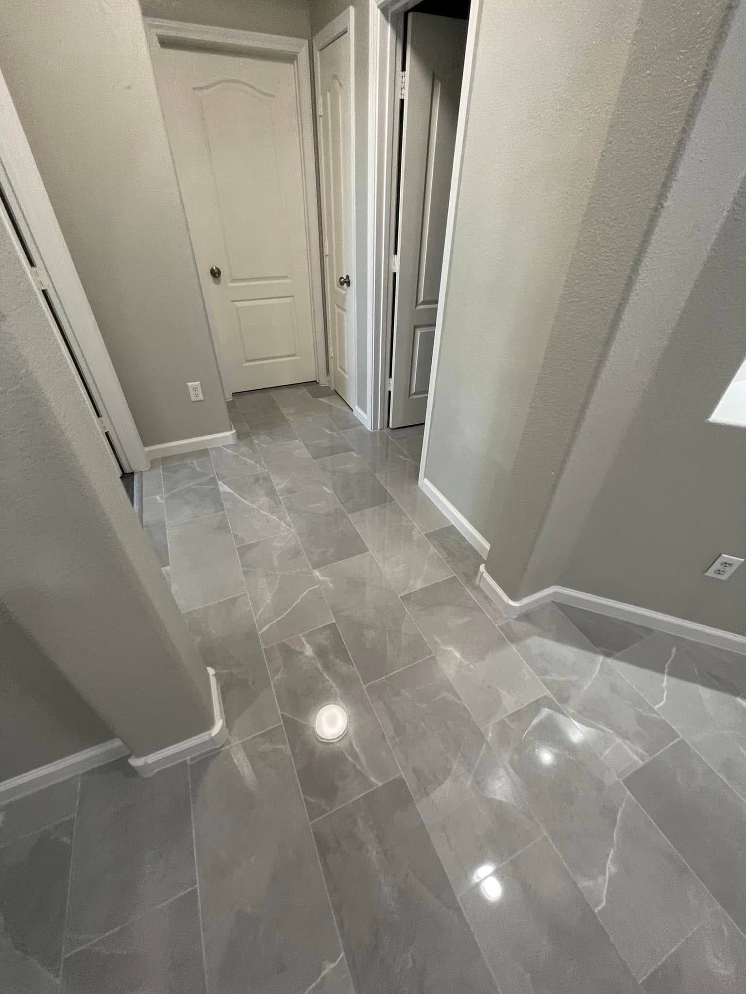 Empty tiled hallway with white doors and gray walls, viewed from a doorway.