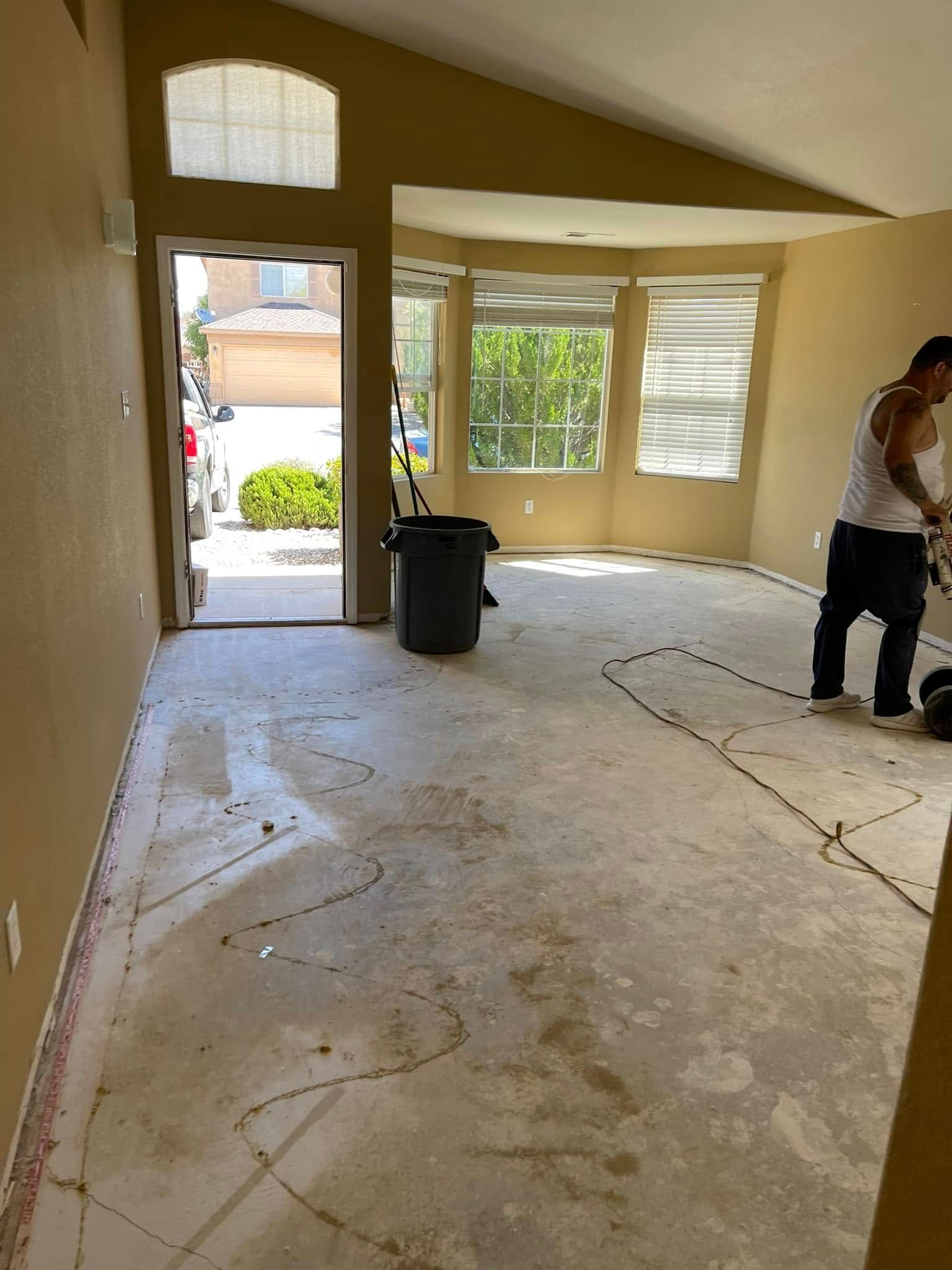 Empty room with stripped flooring, open front door, and a person working near the right wall.
