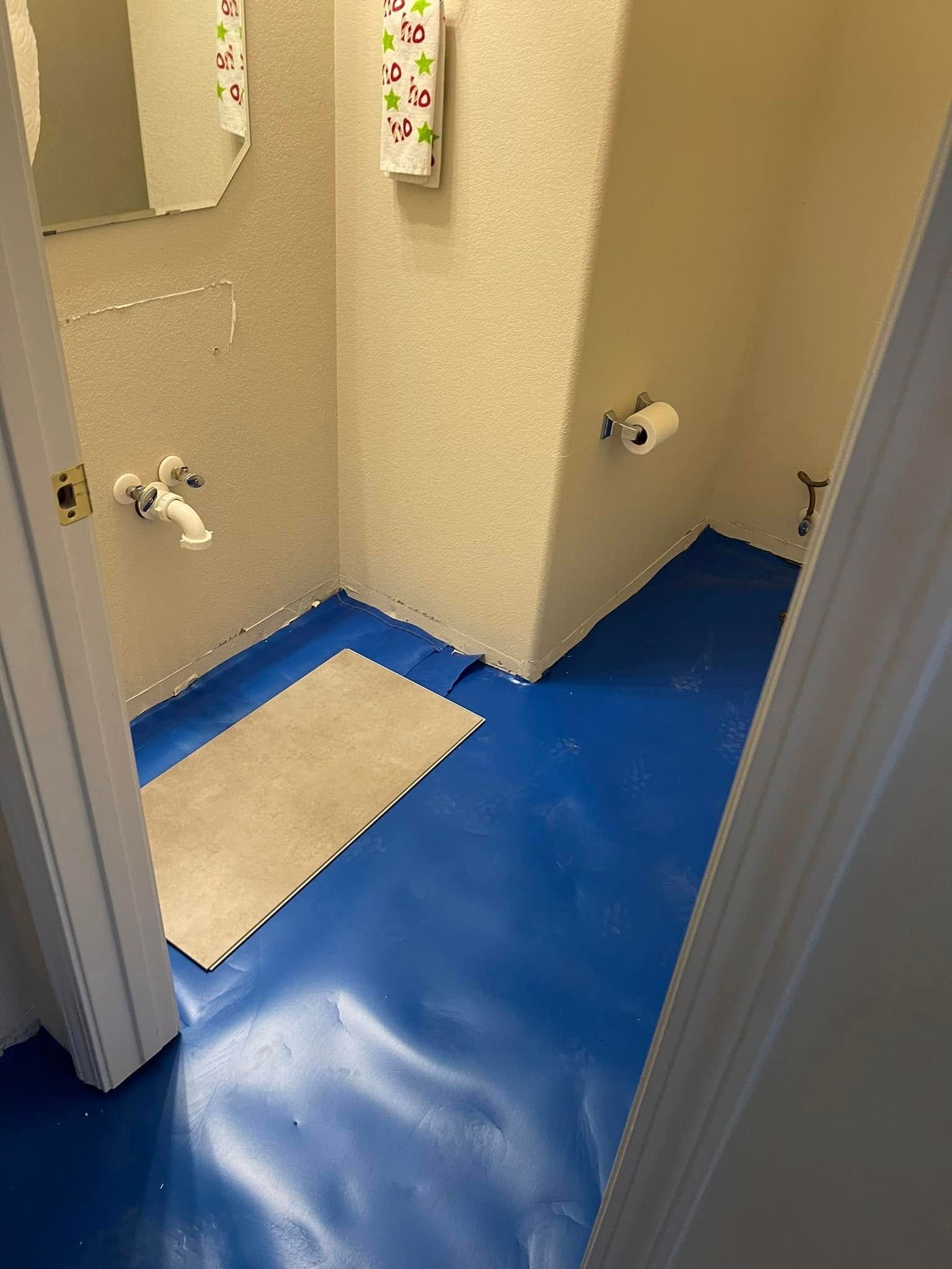 Small restroom area with blue floor, beige walls, two sinks, and a torn floor mat near the doorway