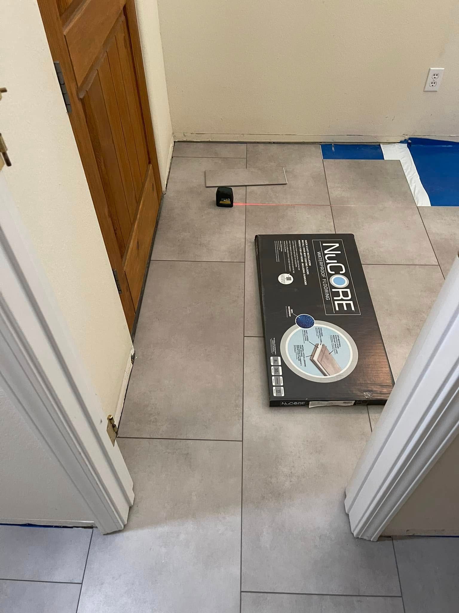 Hallway with a black box on the floor near a door and a loose cable on the tile.