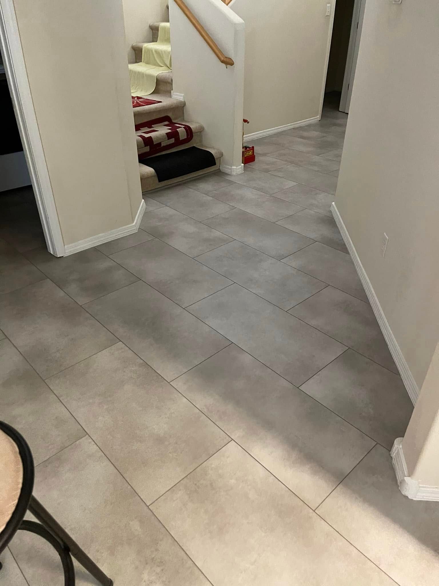 Empty hallway with light gray tile floors and white walls, viewed toward a doorway and stairway.