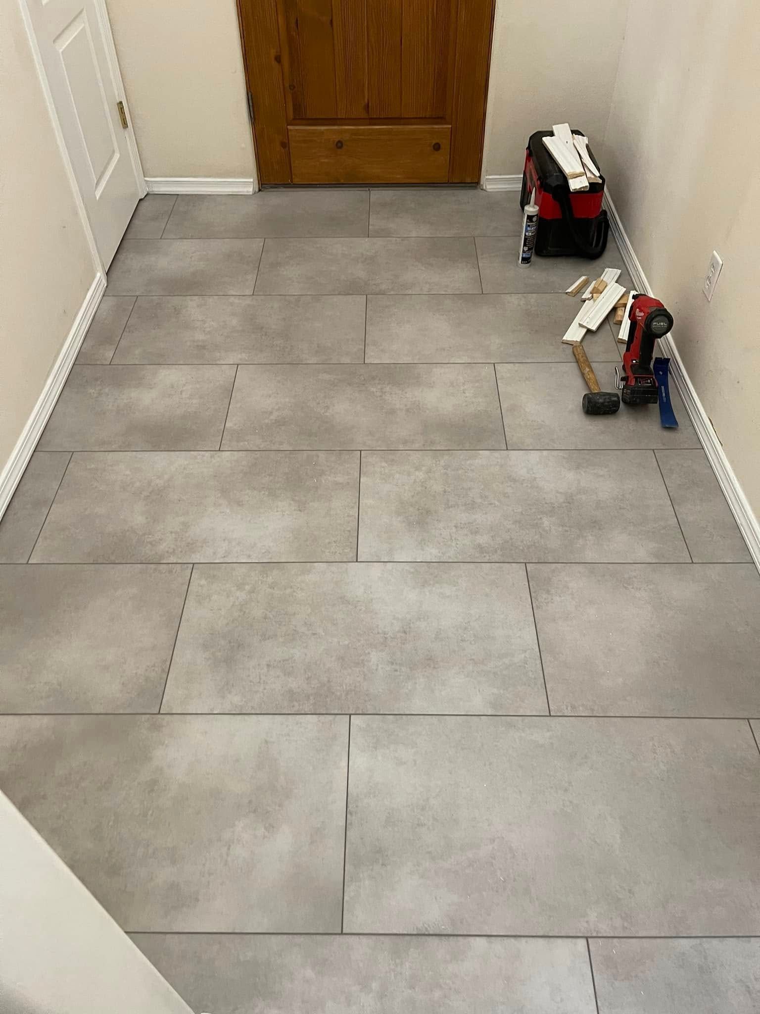 Gray tiled hallway with a wooden door and two small toys along the right wall.