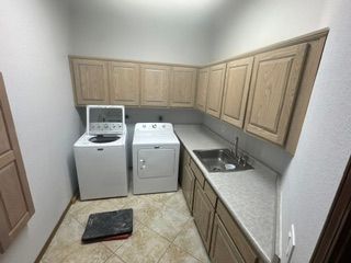 Small laundry room with white washer, dryer, sink, and wood cabinets along both walls.